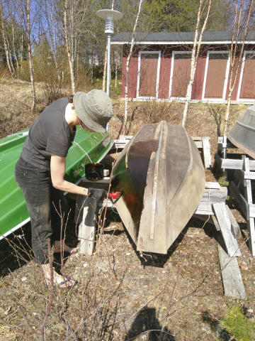Person applying tar on a wooden boat with a brush