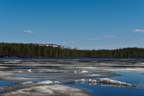 Ice remnants floating on lake with partly snow covered fell in background