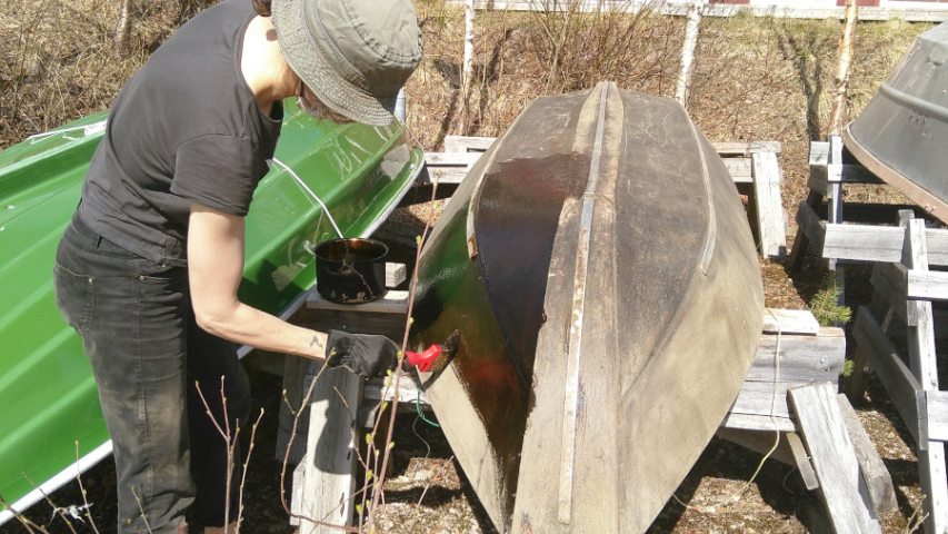 Person applying tar on a wooden boat with a brush
