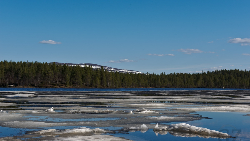Ice remnants floating on lake with partly snow covered fell in background